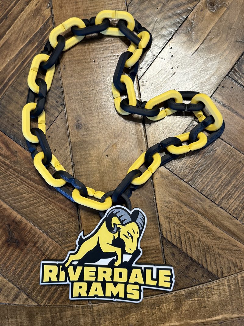Riverdale Rams hype chain: a chunky 3D-printed chain of alternating yellow and black links, with a black ring holding a yellow, black and white Riverdale Rams ram logo medallion, laid on a wood floor.